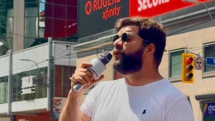 Orgun Ozar sur un coin de rue en ville parlant à un micro.