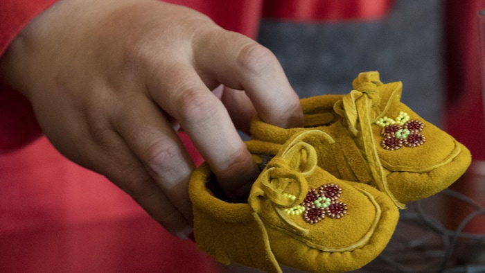 Une main tient des petits mocassins jaunâtres.