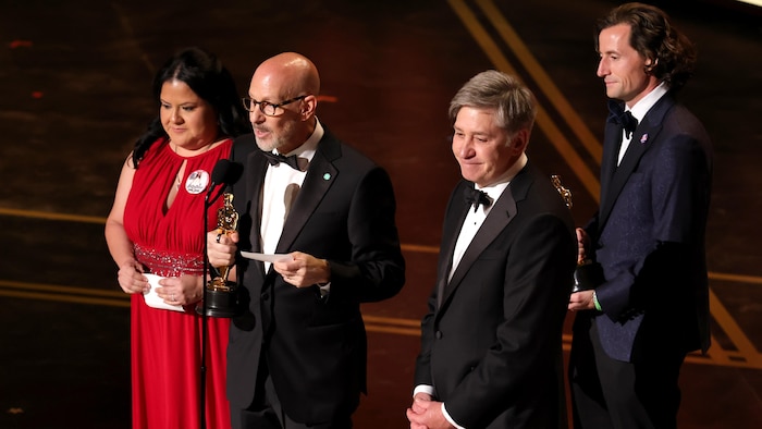 Trois hommes et une femme sont sur scène. 