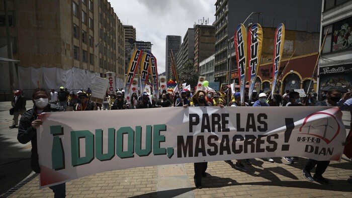Manifestantes sostienen una pancarta con un mensaje que dice en español: "Duque, pare las masacres", dirigido al presidente de Colombia, Iván Duque, mientras marchan hacia la Plaza de Bolívar en Bogotá, Colombia, el miércoles 12 de mayo de 2021.