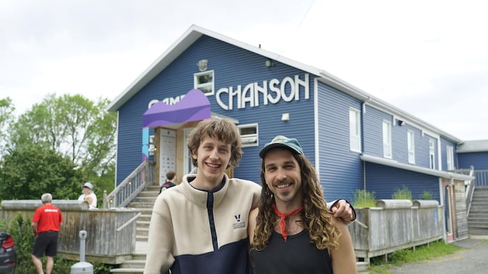Deux jeunes hommes se tiennent par l'épaule et regardent l'objectif en souriant devant le camp chanson.
