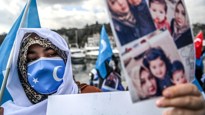 Una mujer enmascarada sostiene fotos de niños y una bandera.