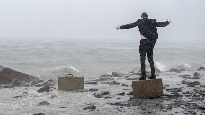Un homme debout sur un morceau de béton fait face à l'océan et aux vents violents.