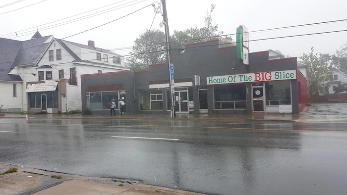 Deux hommes vêtus de sacs poubelle marchent contre le vent et la pluie.
