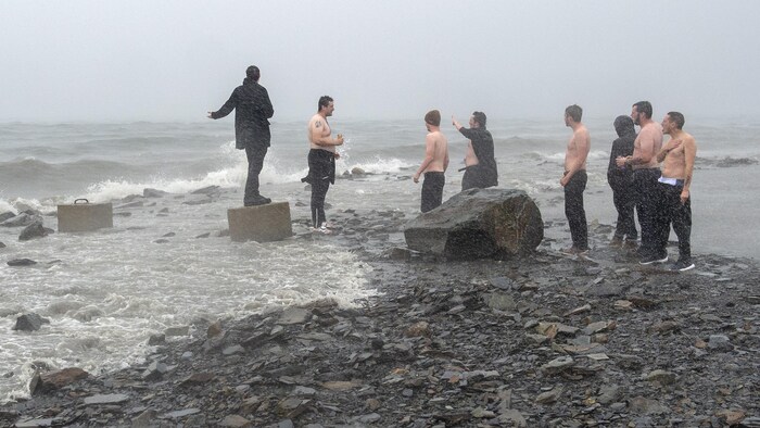 Un groupe d'hommes, plusieurs sans leur chemise, se tiennent près de l'eau dans le port d'Halifax alors que l'ouragan Dorian s'approche.