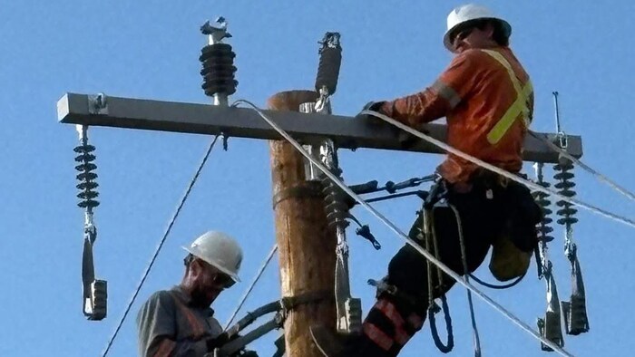 Deux hommes sur le même poteau d'électricité.