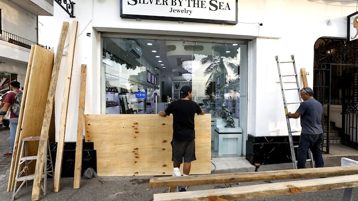 Des hommes installent des planches de bois pour protéger les commerces du secteur contre les répercussions potentielles de l'ouragan Simon.