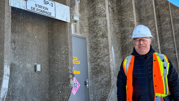 Un homme avec un casque de construction devant une station de pompage. 