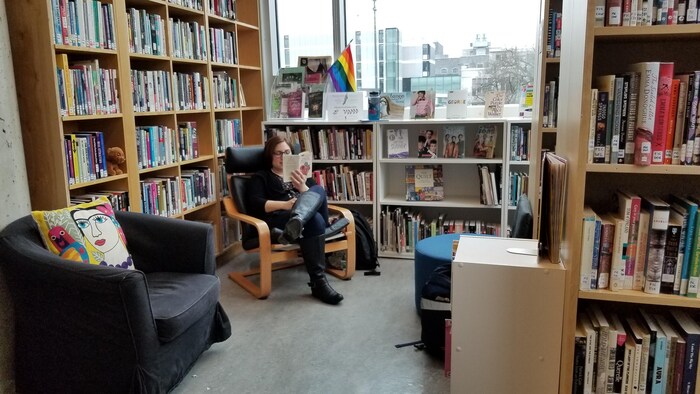 Une personne lit, assise dans un fauteuil, dans la blbliothèque queer Out on the Shelves, à Vancouver.