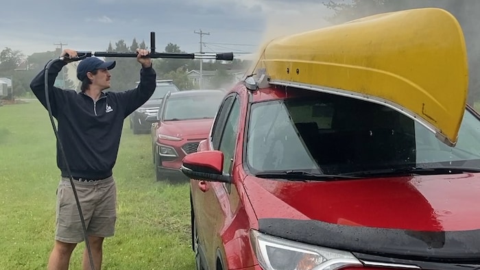 Un homme lave un canot sur le toit d'une voiture à l'aide d'un boyau à haute pression.