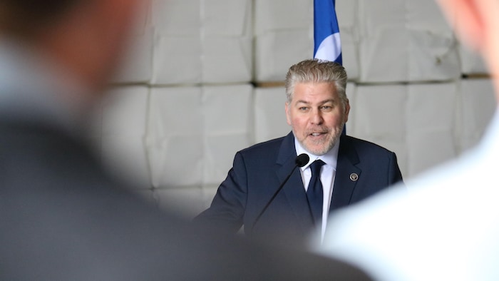 L'élu Pascal Bérubé, en costume derrière en chevalet, s'adresse à une foule dont on apperçoit deux épaules au premier plan.