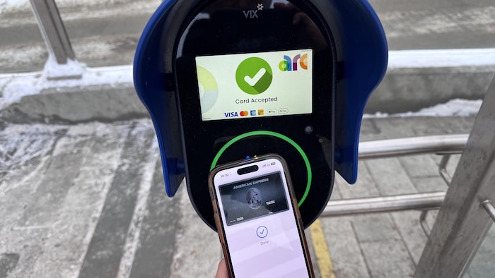 Un usager pointe son téléphone sur une borne pour un paiement électronique sans contact.