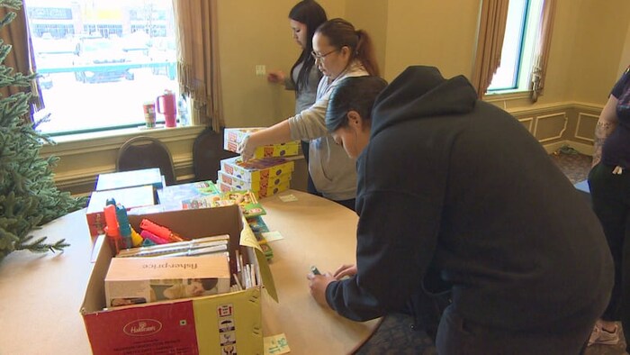 Paige Paupanakis numérote une boîte remplie de jeux pour enfants sur une table accompagnée de deux autres personnes.