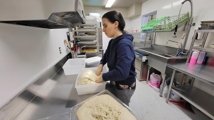 Une femme pétrit de la pâte à pain debout dans une cuisine industrielle.