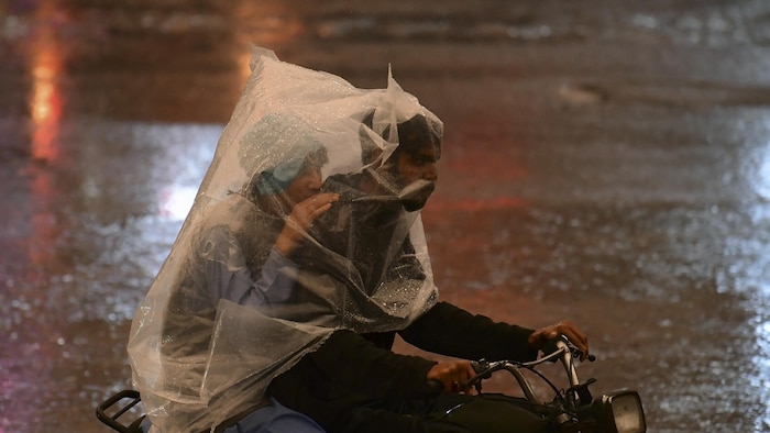 Deux Pakistanais roulent à moto dans une rue inondée, enveloppés d'un sac de plastique pour se protéger de la pluie.