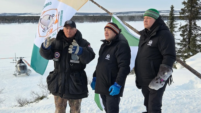 Trois hommes debout devant des drapeaux en plein hiver.