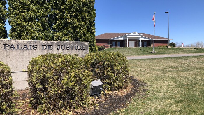 Un bloc de béton sur lesquels les mots « Palais de justice » sont gravés et un édifice plus loin derrière.