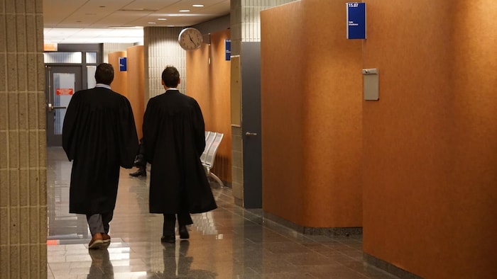 Des avocats en toge marchent, de dos, dans un couloir du palais de justice de Montréal.