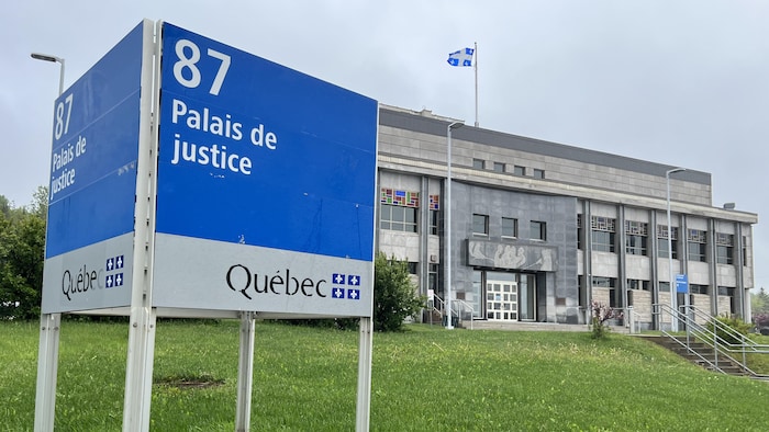 Extérieur du bâtiment. On voit le panneau à l'entrée du bâtiment sur lequel il est écrit 87, Palais de justice.