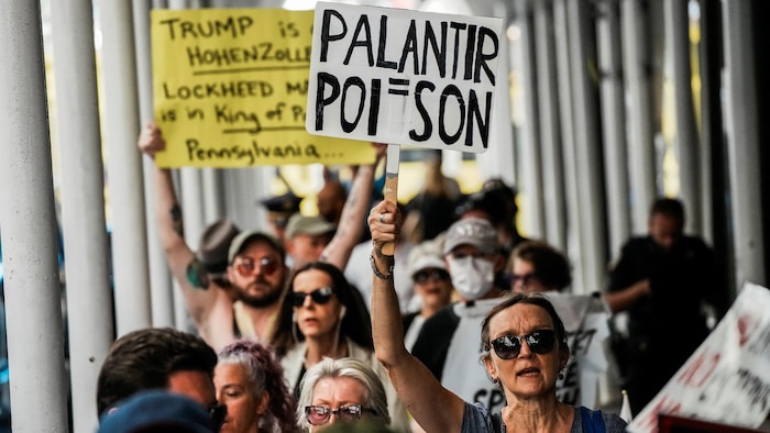 Des manifestants protestent contre Palantir, une femme brandit une affiche disant Palantir égale poison.