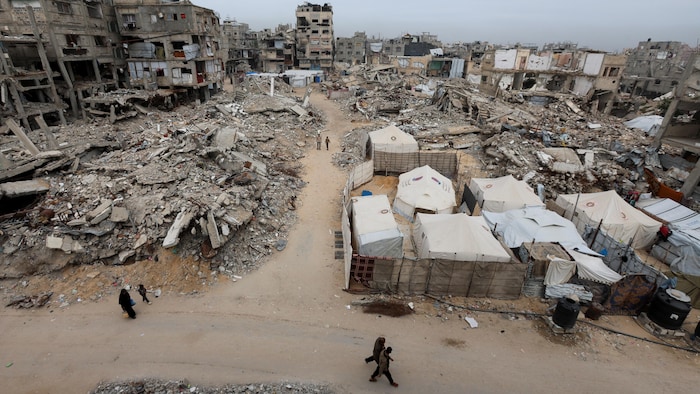 Palestinians walk past the rubble of apartment buildings destroyed by the war.