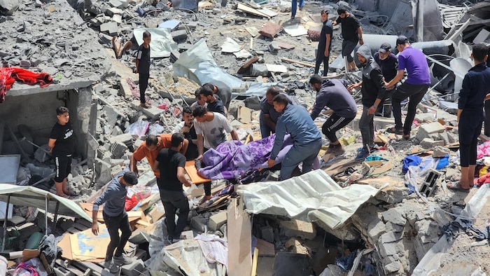 Des Palestiniens qui marchent dans les débris d'une maison détruite portent le corps d'une personne tuée.