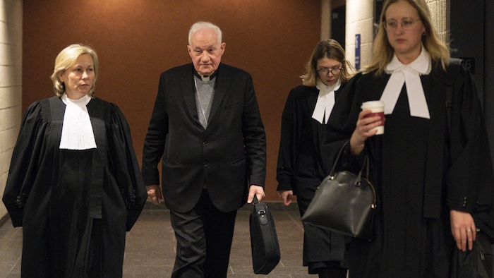Le cardinal marche dans un corridor du palais de justice de Montréal en compagnie de ses avocates.