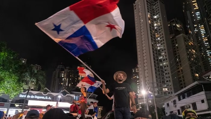 Des manifestants la nuit agitent des drapeaux du Panama.