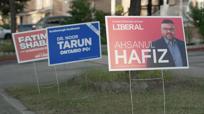 Trois pancartes des partis néodémocrate, progressiste-conservateur et libéral partagent le même carré d’herbe dans une rue de banlieue.