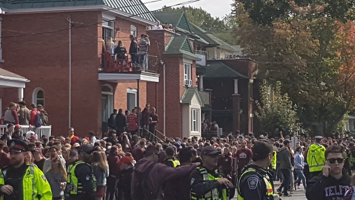 Une grande foule dans la rue avec des agents de police et des personnes sur les balcons des résidences du secteur.