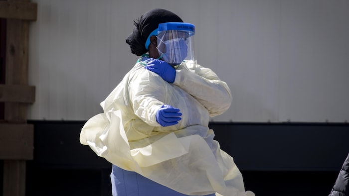 Une femme porte une jaquette de protection, des gants et un masque.