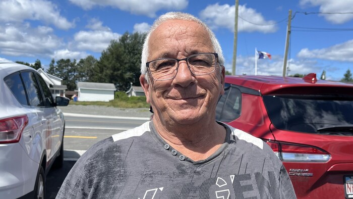 Un homme pose pour une photo, debout dans un stationnement.