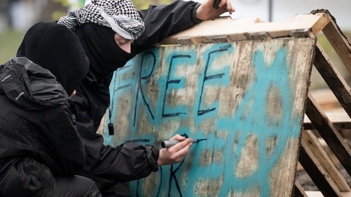 Un manifestant écrit « Magasinage gratuit » sur un panneau en bois.