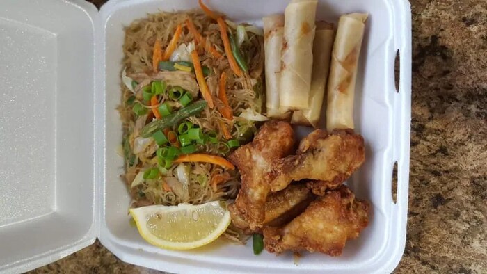 Pansit, lumpia at chicken wings na nakalagay sa styrofoam container.