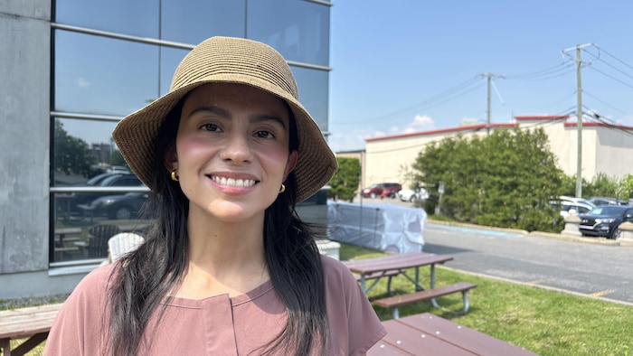 Paola Rey sourit à la caméra, protégée du soleil par un grand chapeau.