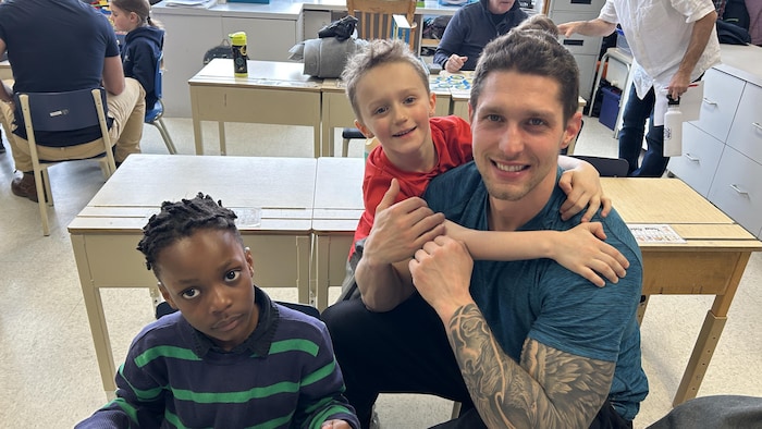 un papa avec son fils et un ami dans une classe.
