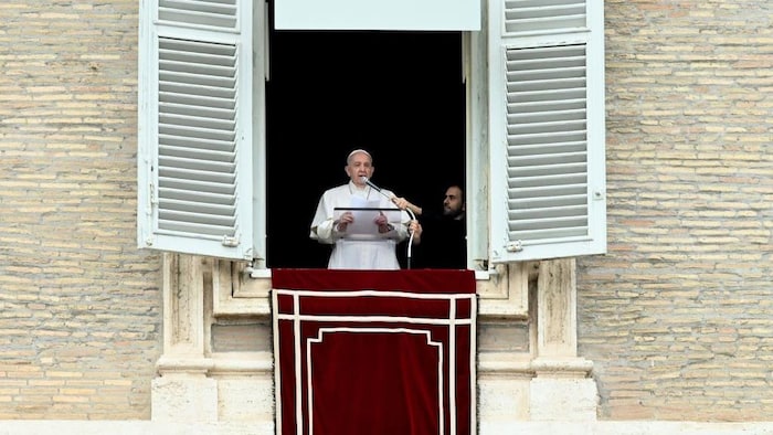 Le pape parle depuis une fenêtre à très grands volets. Un homme tient son micro.