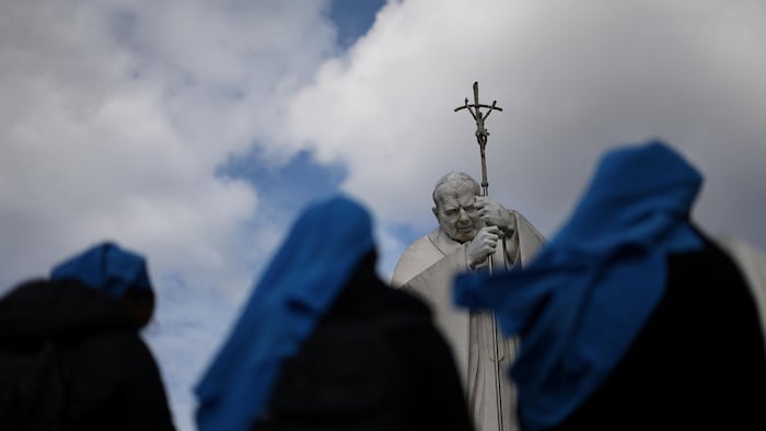 Des religieuses prient à côté de la statue du défunt pape Jean-Paul II.