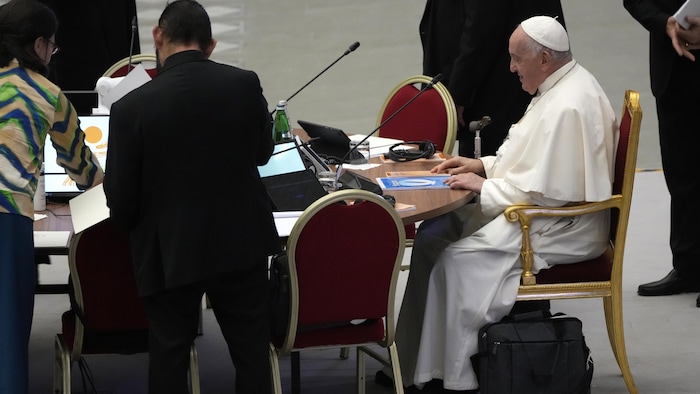 Le pape François est assis devant un bureau.