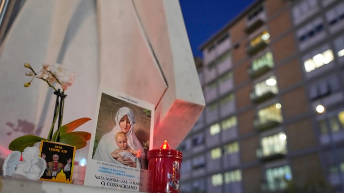 Une image du pape, une bougie et une image de la Vierge Marie reposent au pied d'une statue.