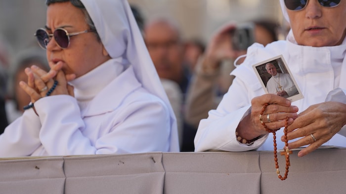 Une religieuse tient une photo du pape et un chapelet lors d'un rassemblement.