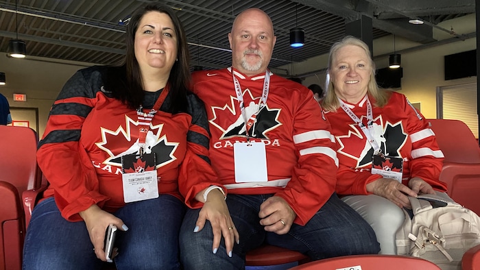 Une maman, un papa et une grand-maman vêtus des chandails officiels rouges d'Équipe Canada.