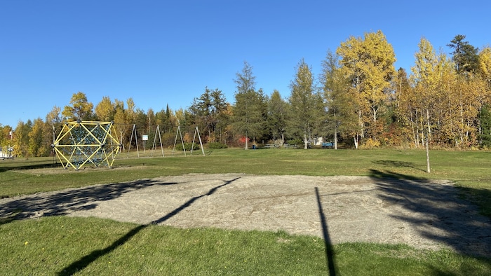 Un parc où on voit un grand carré de gravelle dans le gazon.