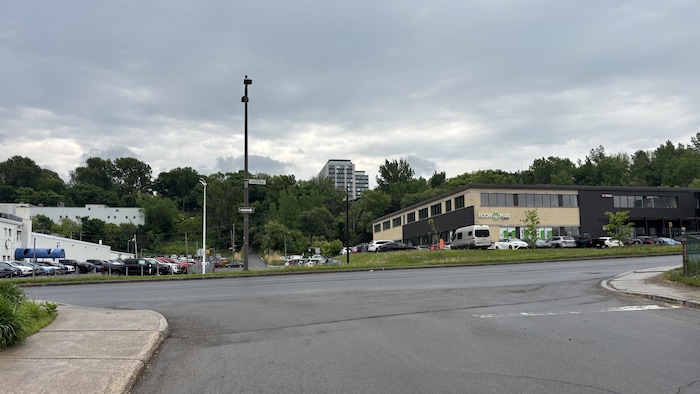 Vue d'un carrefour routier dans le parc industriel Saint-Malo sous un ciel gris et nuageux. À droite, un bâtiment moderne de deux étages, de couleur sombre avec des touches claires, abrite des entreprises. P