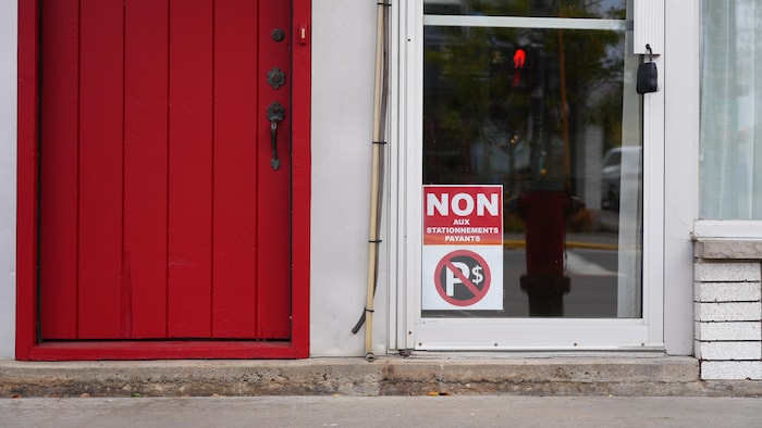 Fenêtre de commerce avec une affiche montrant une croix sur une enseigne de stationnement.