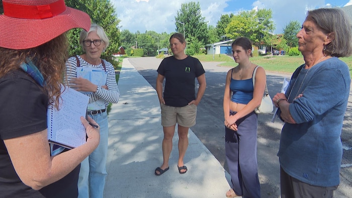 Cinq dames discutent sur un trottoir.