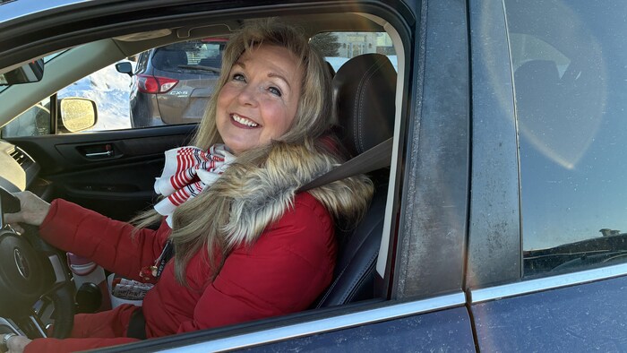 Une femme en voiture sourit à la caméra.