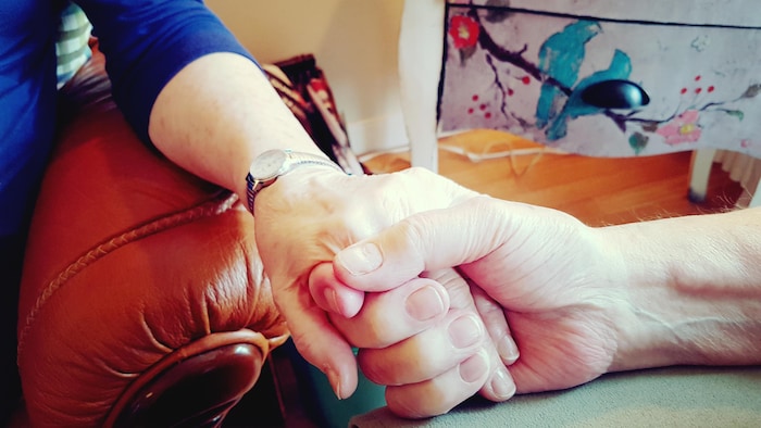 Un proche aidant tient la main de sa conjointe.