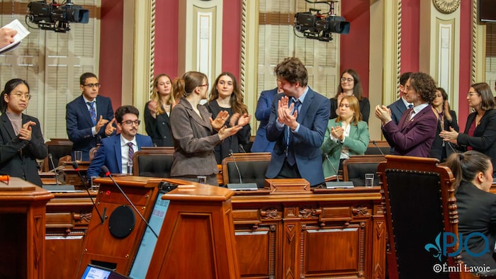 Des députés étudiants sont levés et applaudissent une de leur collègue en chambre.