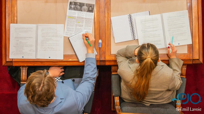 Deux personnes prennent et lisent des notes assis à un bureau. ils sont vus d'en-haut.